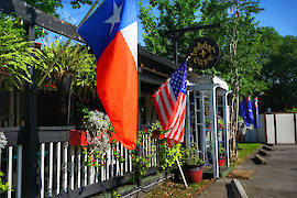 An awning- and fern-bedecked veranda, with prominent flags, including those of Texas and the United States